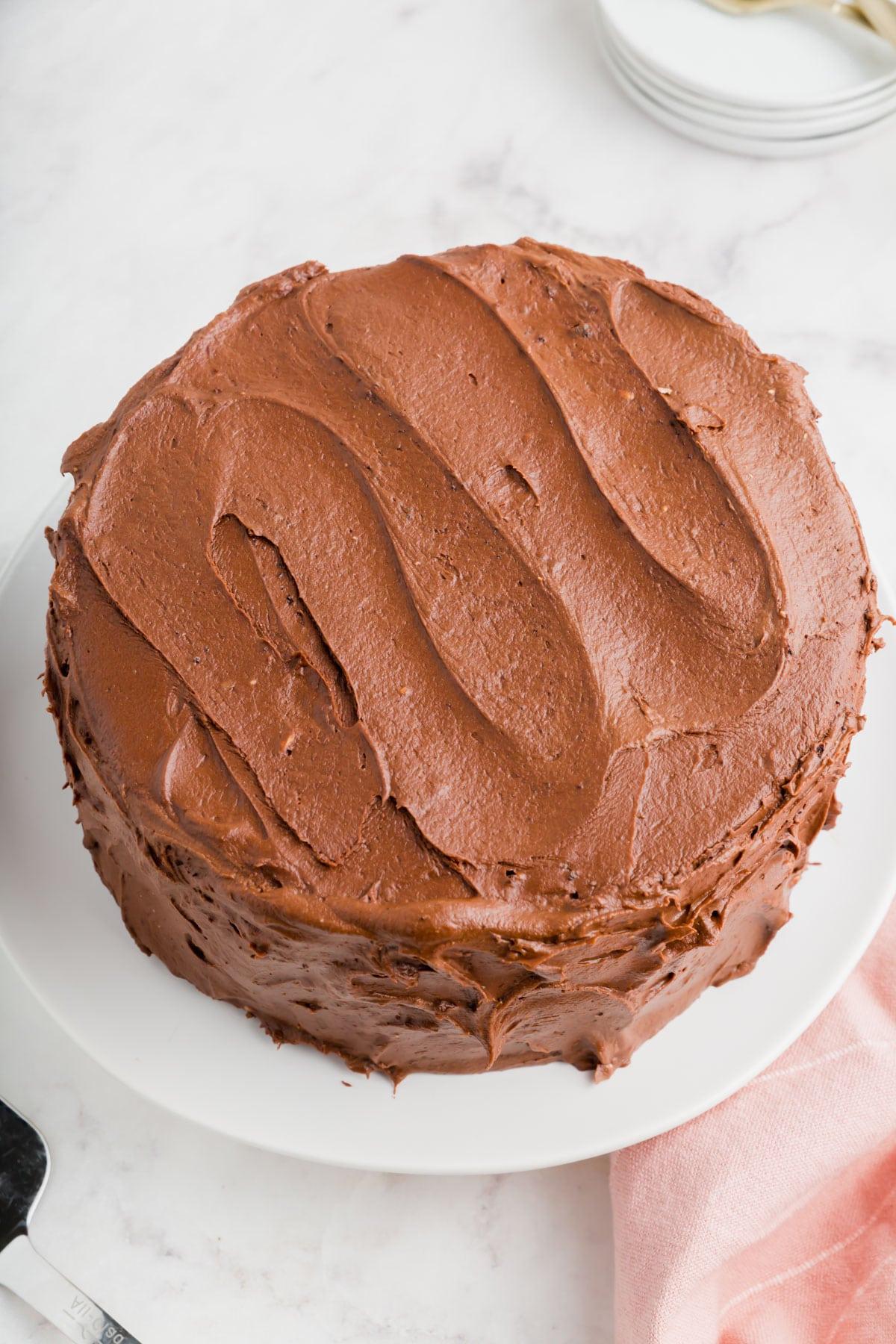 A gluten-free chocolate cake with chocolate frosting on a cake stand.
