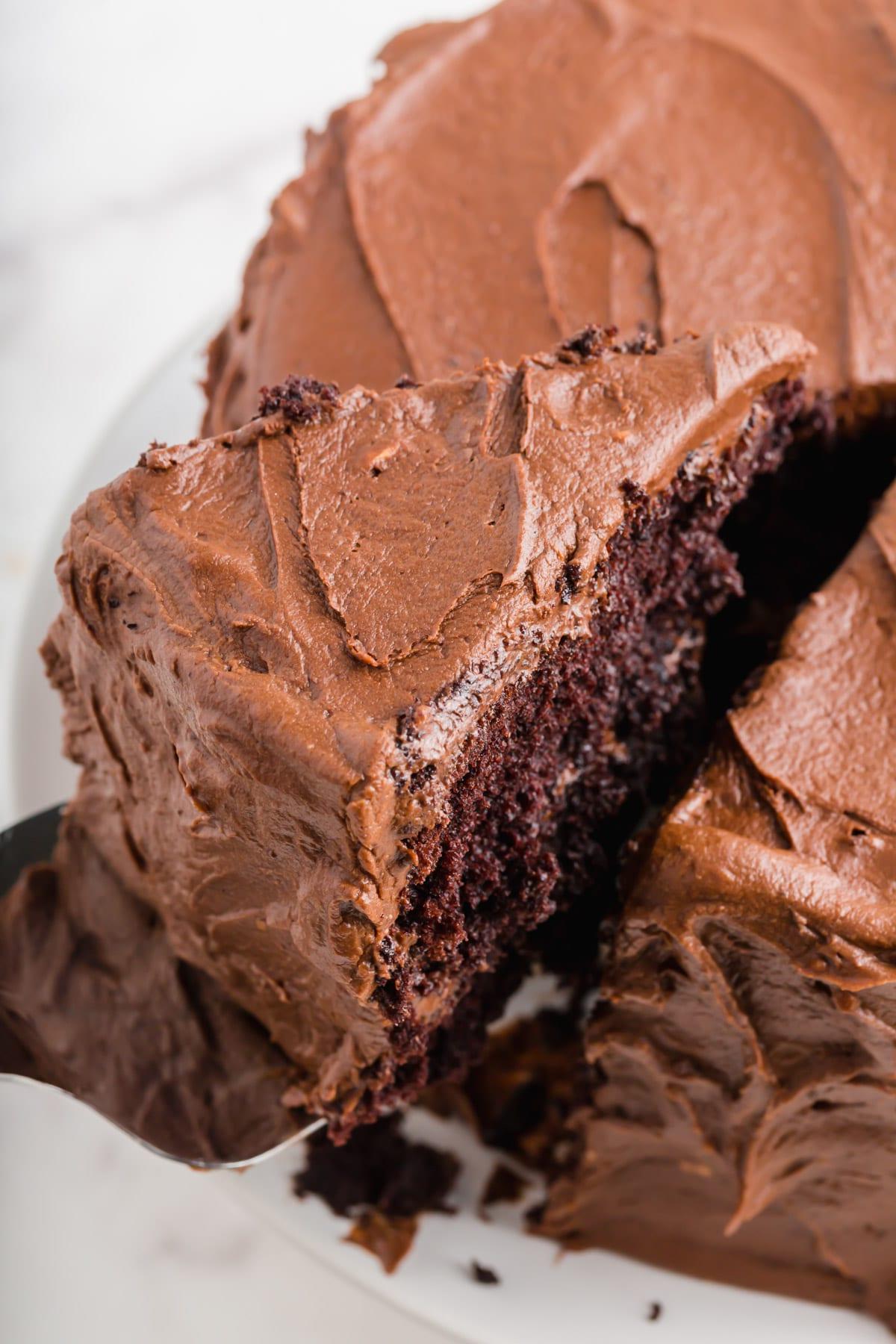 A slice of a gluten-free chocolate cake with chocolate frosting being lifted from the cake.