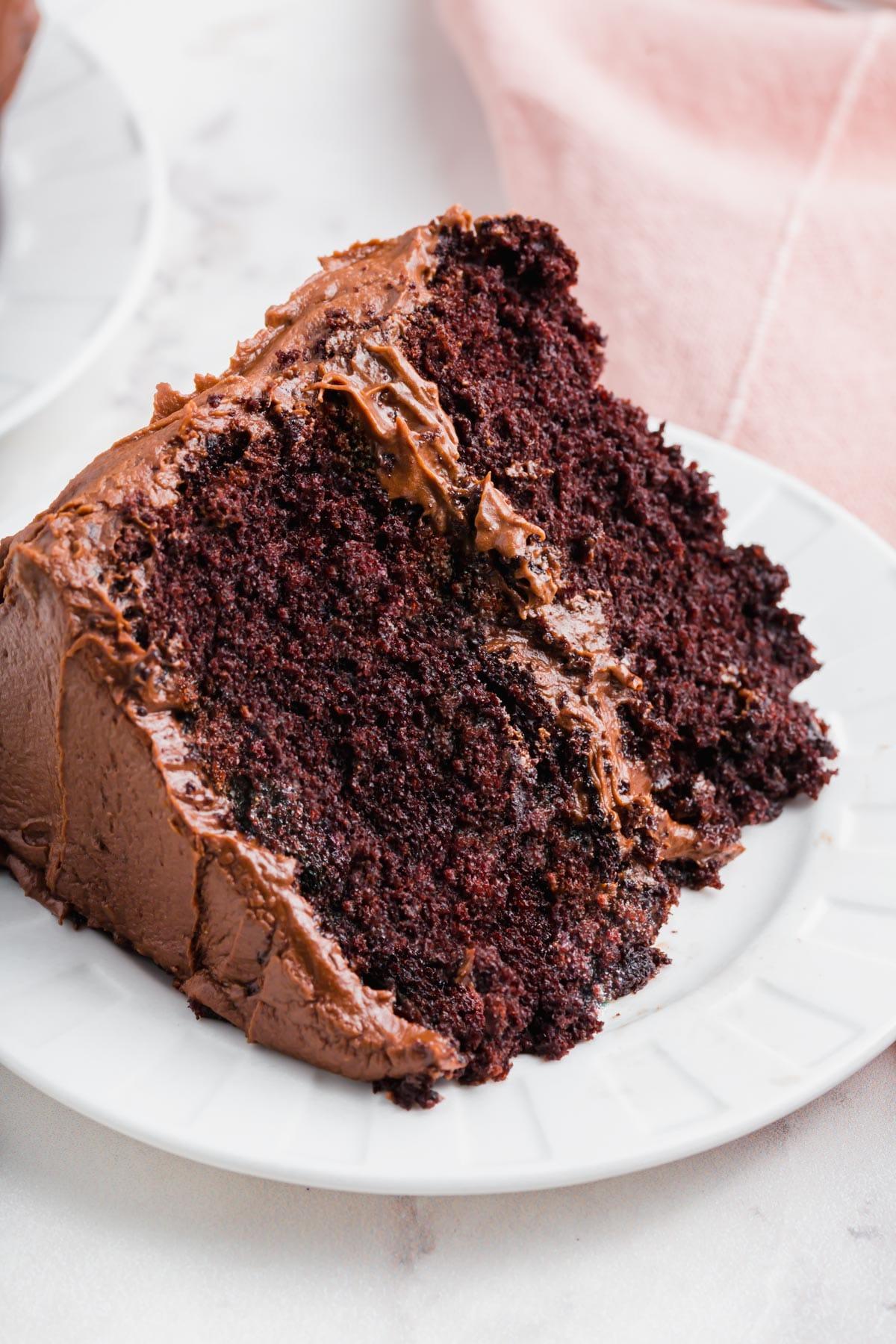 A slice of a gluten-free chocolate cake with chocolate frosting on a plate.