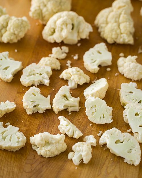 Scattered cauliflower florets on a cutting board.