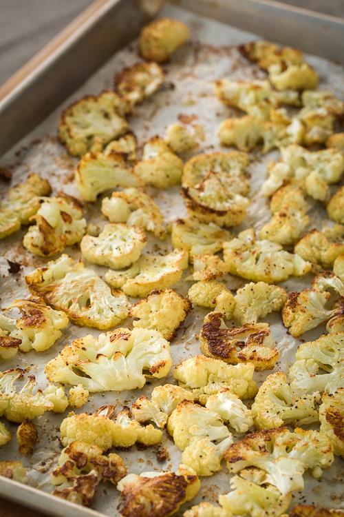 Golden roasted cauliflower florets on a sheet tray lined with parchment paper.