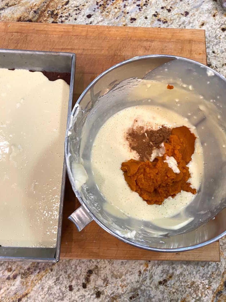 Pumpkin mixture and spices in a mixing bowl next to a pan of cream cheese batter.