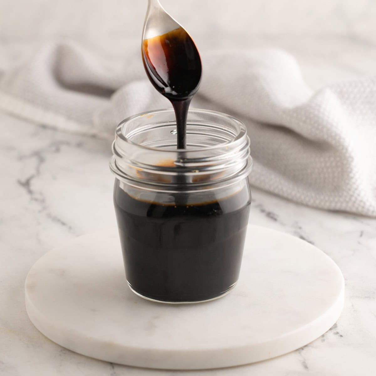 Balsamic glaze dripping off a silver and gold spoon into a glass jar.