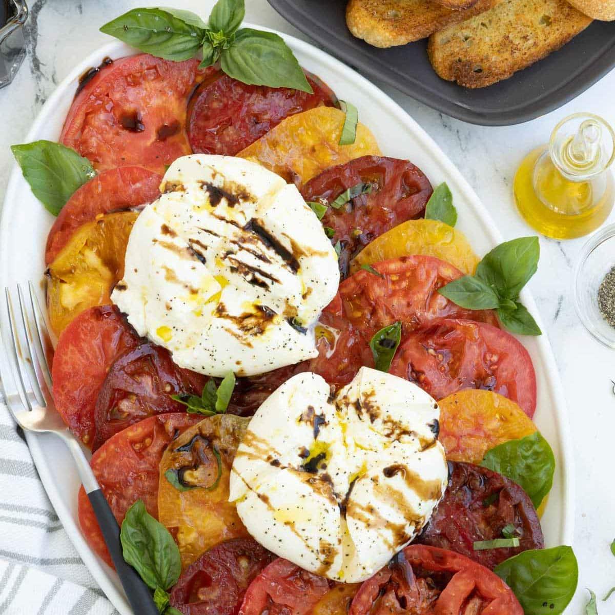 Plate of red, yellow and burgundy tomatoes with burrata and basil.