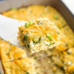 One piece of egg casserole held up by a white spatula over the rest of the casserole.