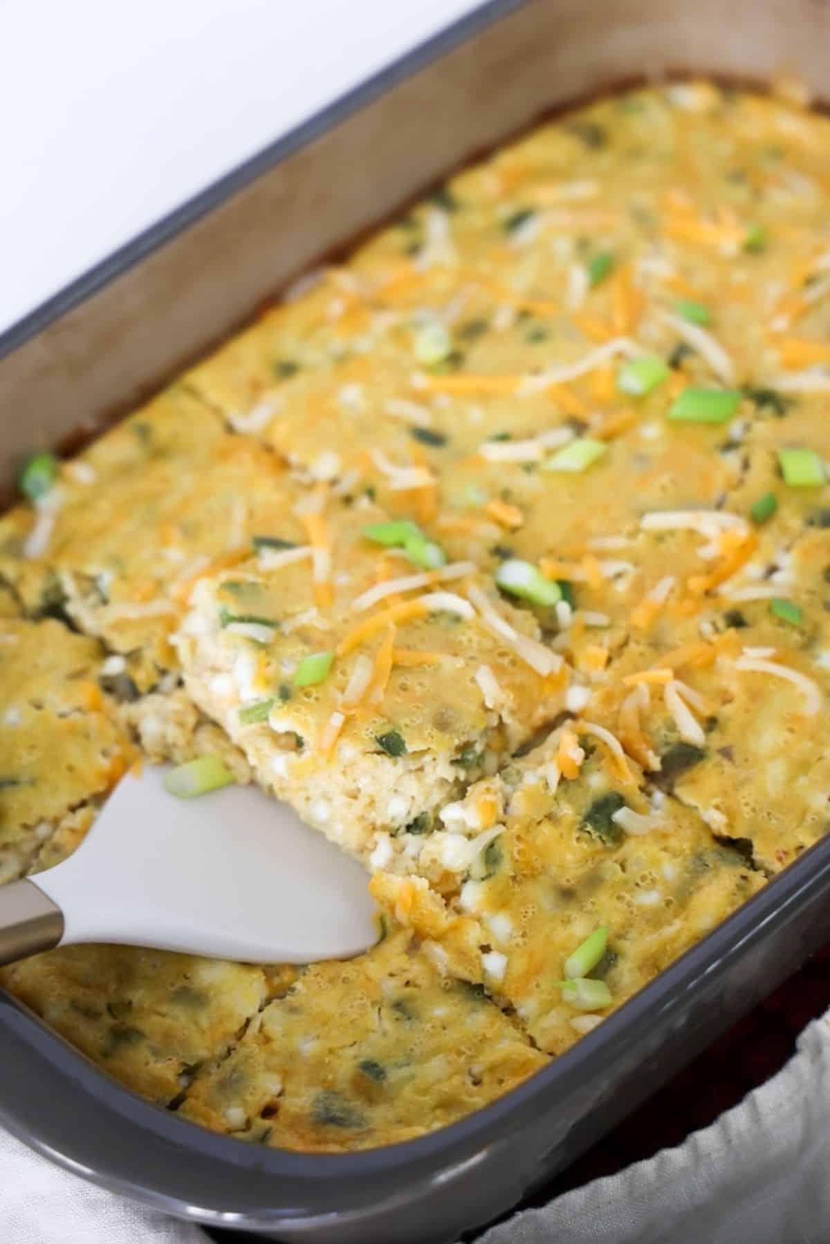 Green chile egg casserole in a large baking dish with one piece being removed with a white and gold spatula.