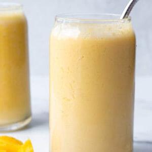 A glass with a yellow smoothie and metal straw.