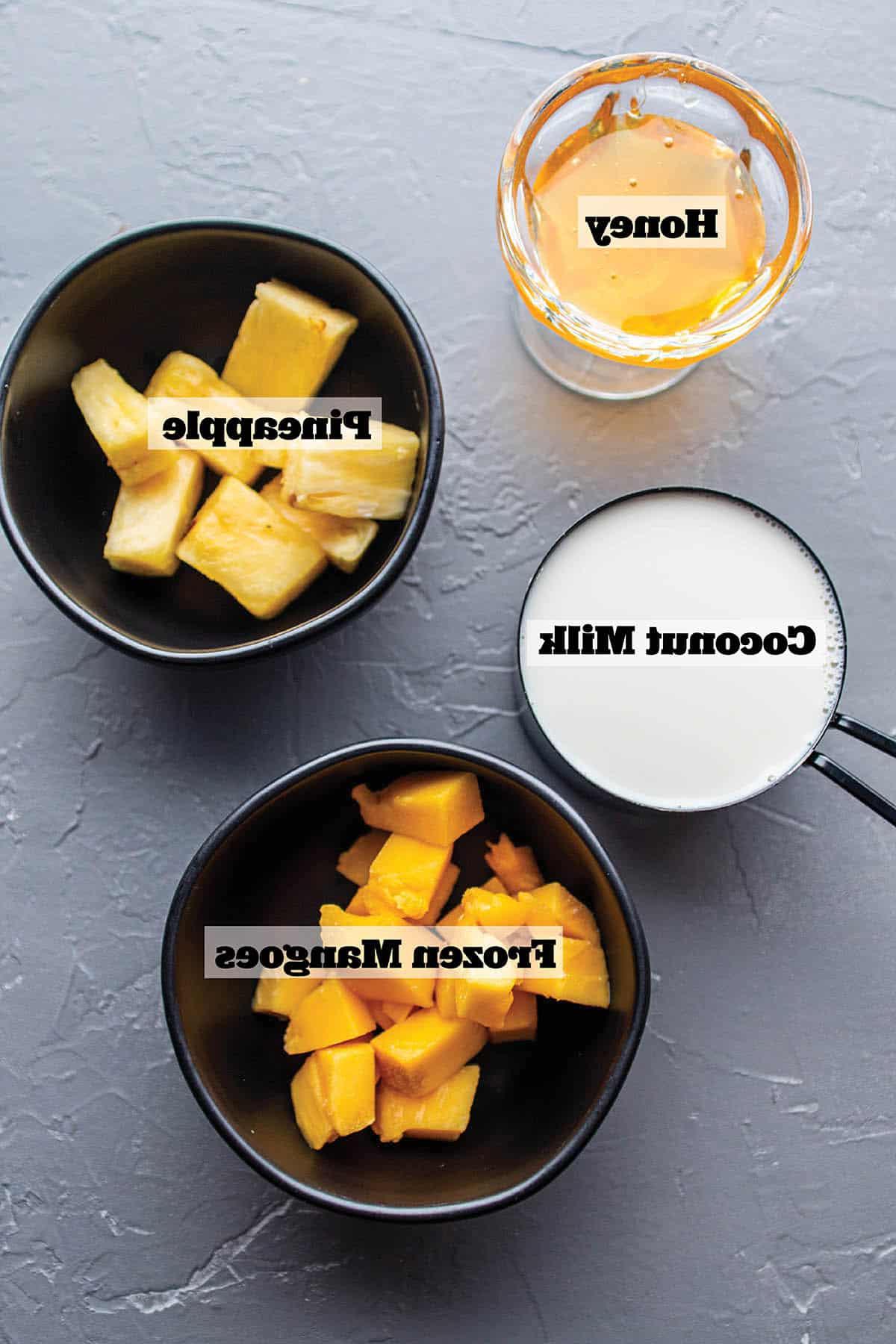 Black bowls with frozen mangoes, pineapple, coconut milk and honey.