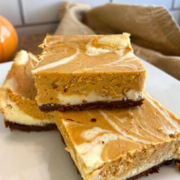 Three pumpkin cheesecake bars stacked on a plate.