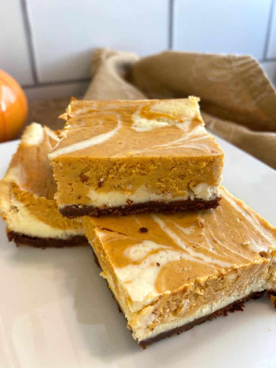 Three pumpkin cheesecake bars stacked on a plate.