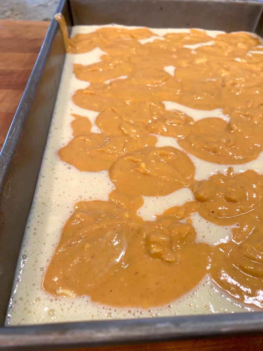 Uncooked batter for pumpkin cheesecake bars in a baking pan.