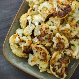 A platter of roasted cauliflower with golden brown edges and parmesan cheese.