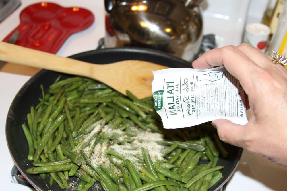 Green Beans Seasoned with Italian Dressing Sautéed green beans in a black fry pan with Good Seasons Italian dressing mix being added